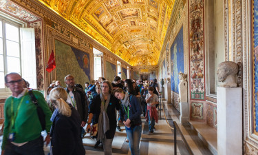 A group of tourists exploring the ornate hallway filled with colorful murals and intricate statues, with an intricately painted ceiling that includes various ancient figures and symbols, within the Sistine Chapel at the Vatican.